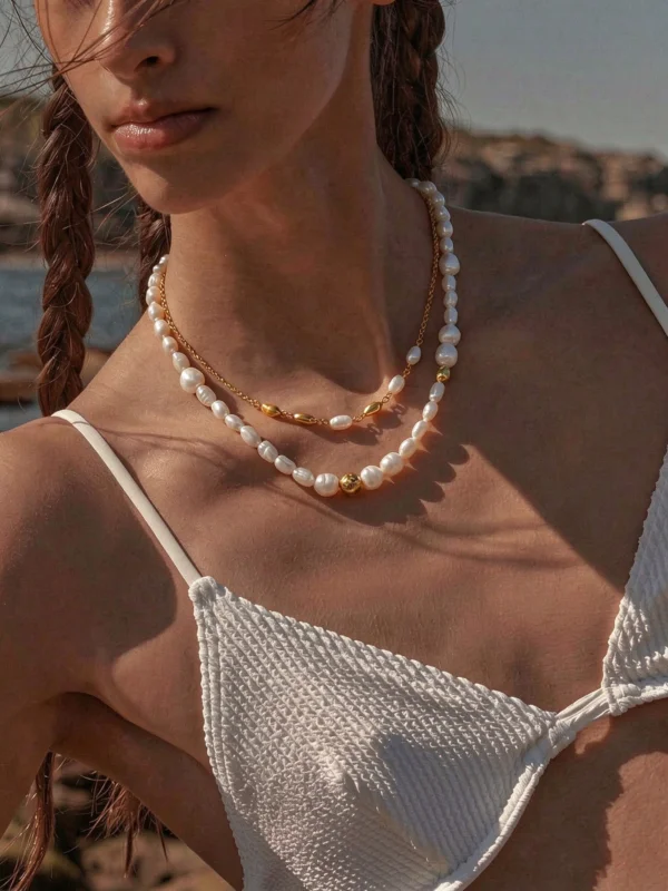 Model wearing two layered freshwater pearl necklaces with gold-tone details