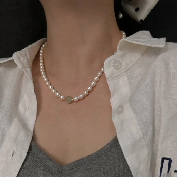 Woman wearing a white freshwater pearl necklace with a round jade accent bead